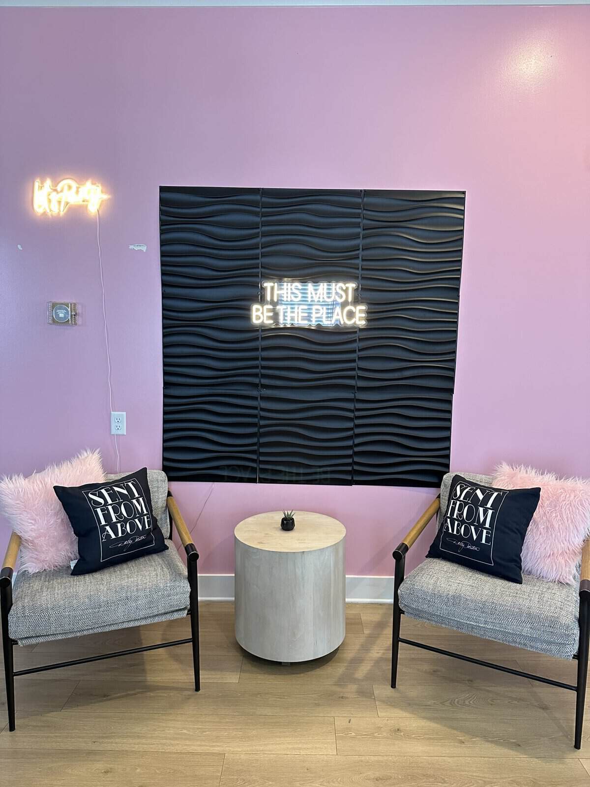 nashville_bachelorette_bnb - Adventures with Carli seating area with two chairs holding one pink and one black pillow. with pink walls and and a neon sign reading"this must be the place"