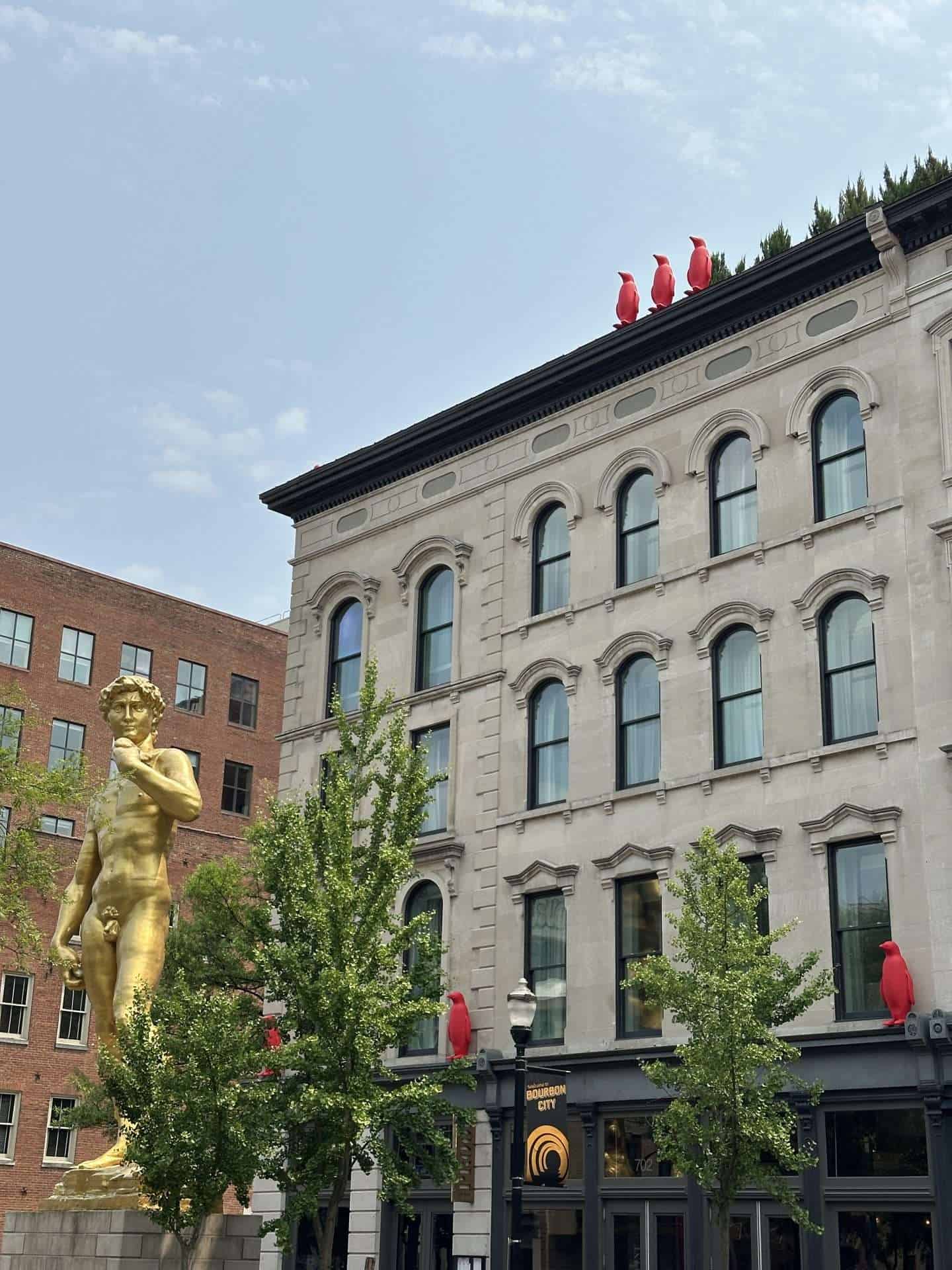exterior of 21c hotel with gold david statue and red plastic penguins lining roof.