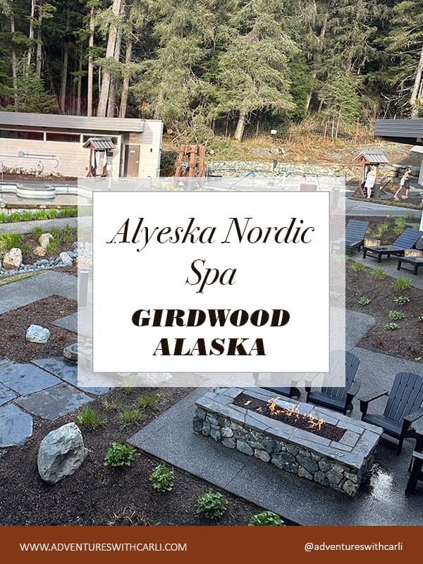 Outdoor Nordic spa in a wooded area with a stone fire pit; foreground sign reads Alyeska Nordic Spa, Girdwood, Alaska.