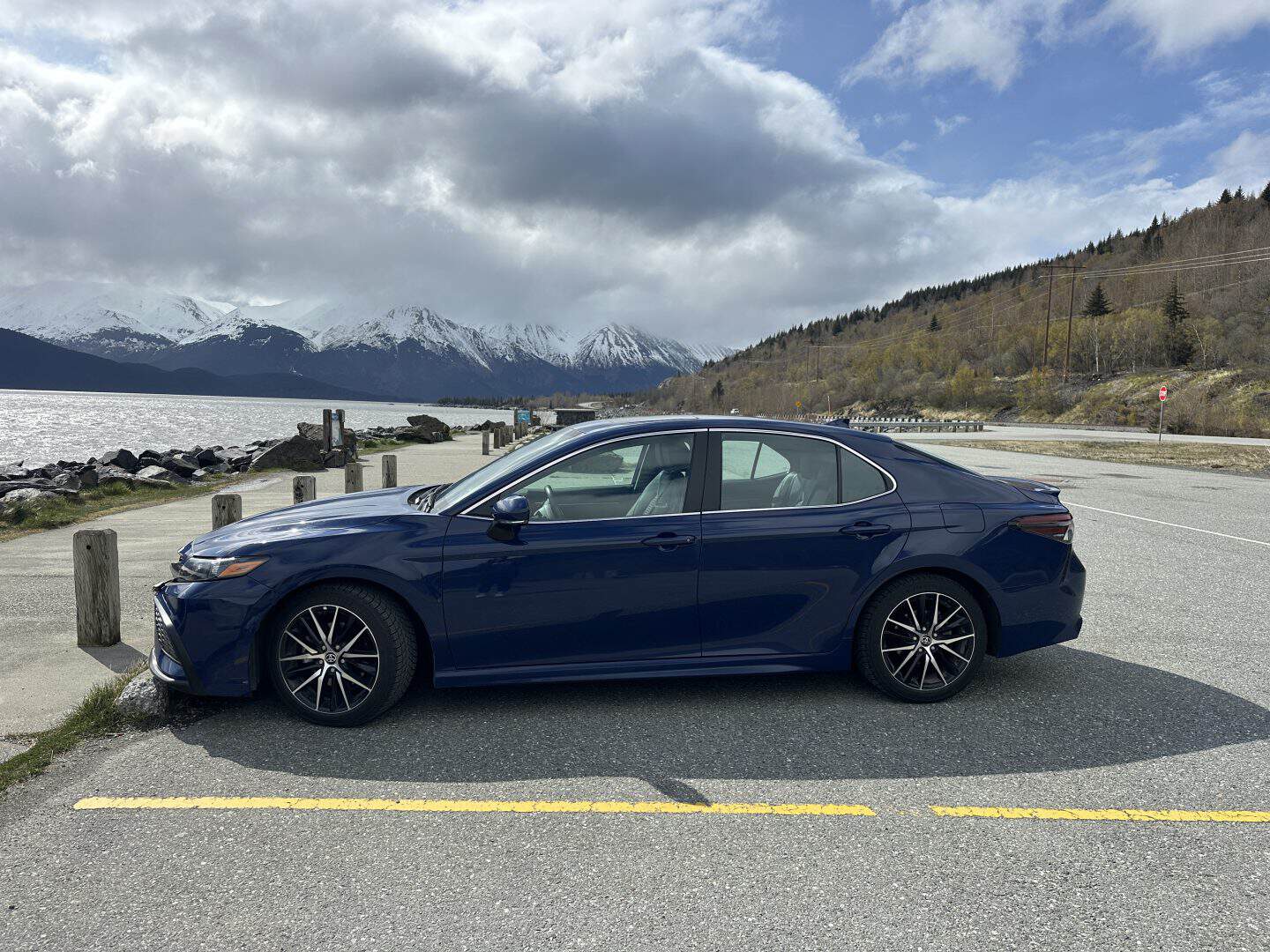 blue rental car parked along  Turnagain Arm, with chugach mountains in background
