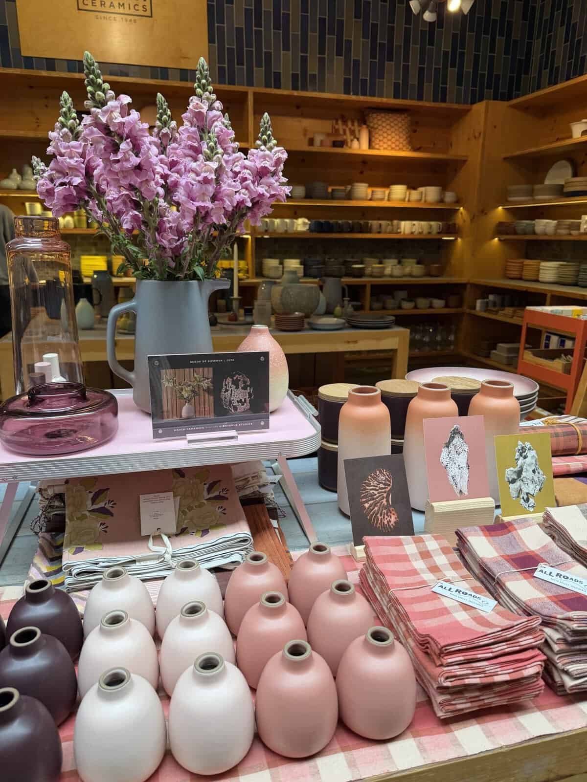 table display of flower bud vases in varying colors of pink next to stacks of pink plaid tea towels