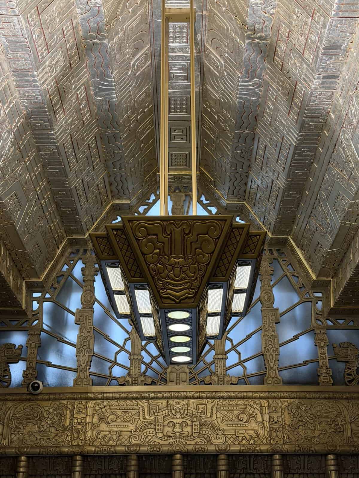 Ornate metal ceiling with geometric patterns and a central gold beam and hanging lanterns.