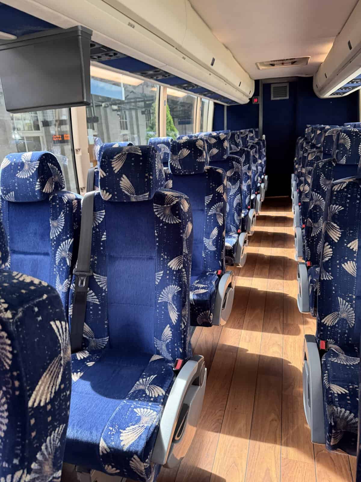 Interior of a bus from seattle to Vancouver airport with rows of blue patterned seats and overhead storage, windowed side showing outside city street.