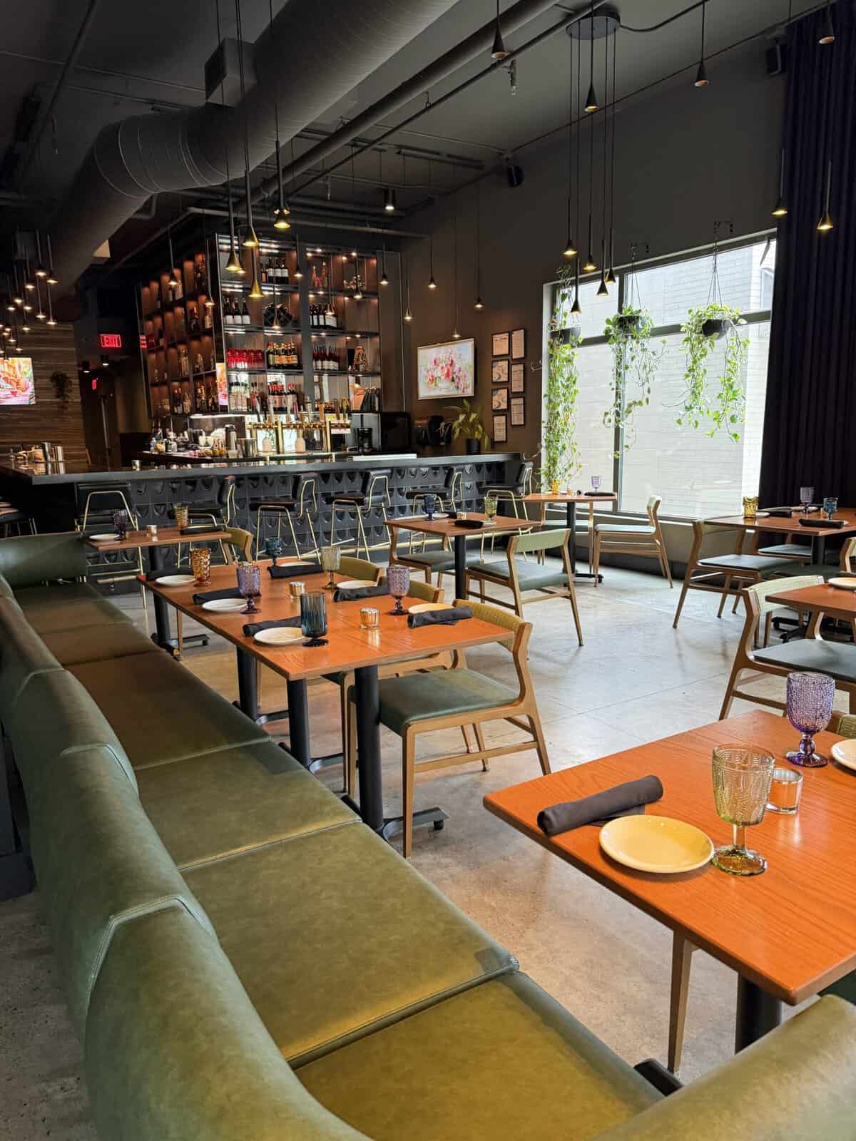 Modern restaurant interior with a long bar, pendant lights, and wooden tables set for service.