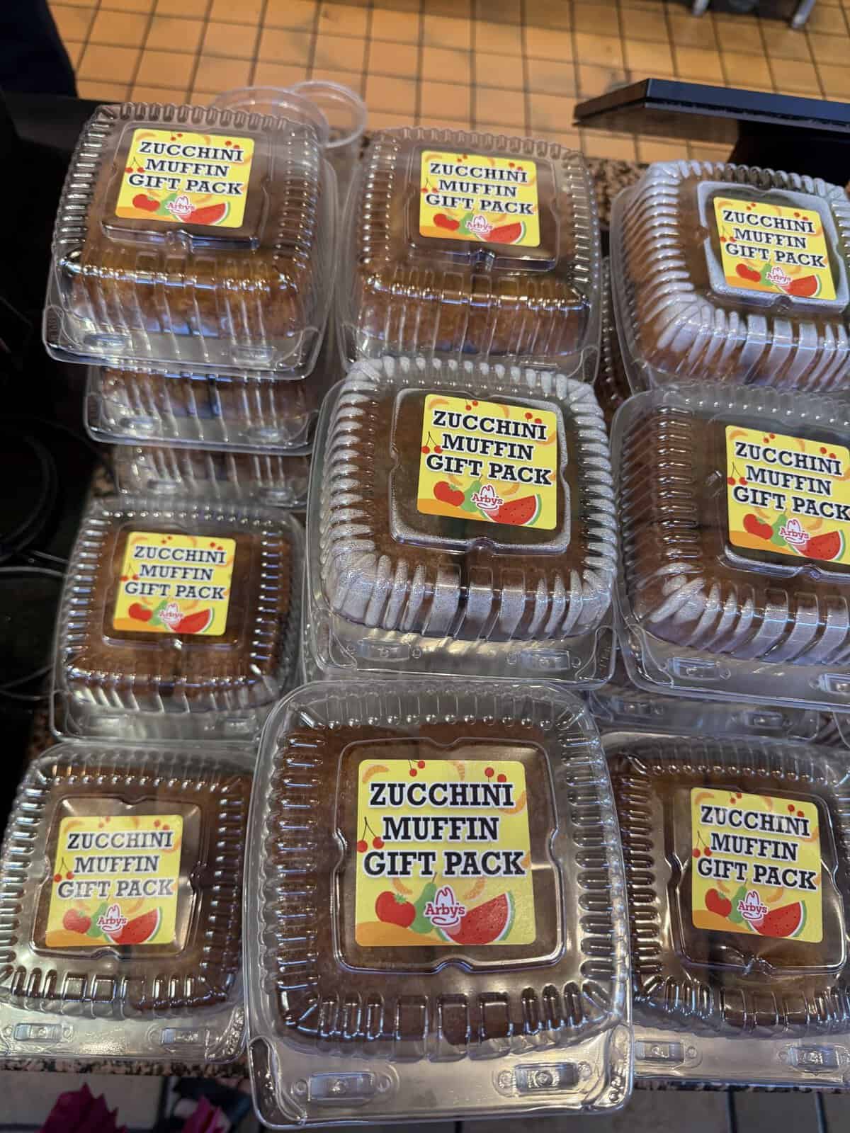 Stack of clear plastic muffin gift packs labeled"Zucchini Muffin Gift Pack" on a display table.