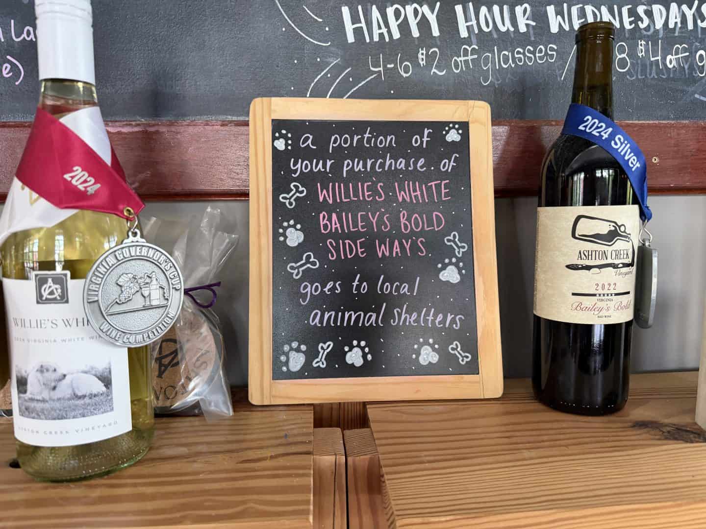 one bottle of wine with medals on each side of a chalkboard dedicating portions of the proceeds for the wine to animal shelters