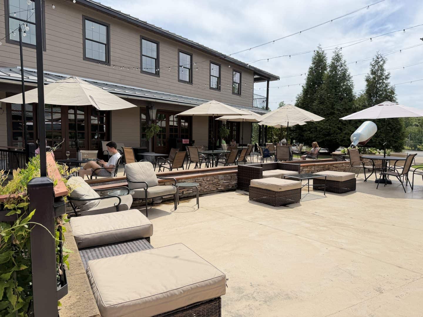 large outdoor patio with black metal  tables and seating with beige cushions and beige sun umbrellas overhead