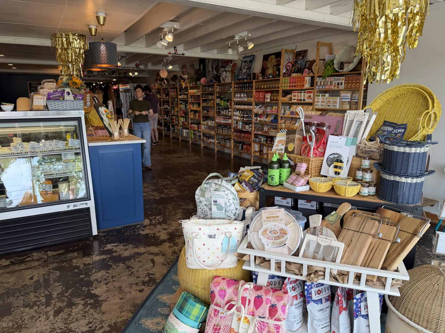 Busy shop interior with shelves of food and home goods, colorful tote bags and baskets in the foreground.