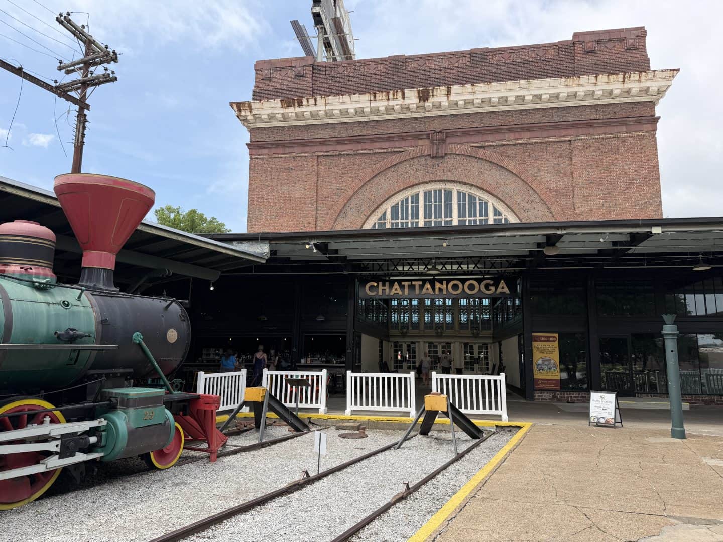 historic brick train station with old steam locamotive on tracks in foreground