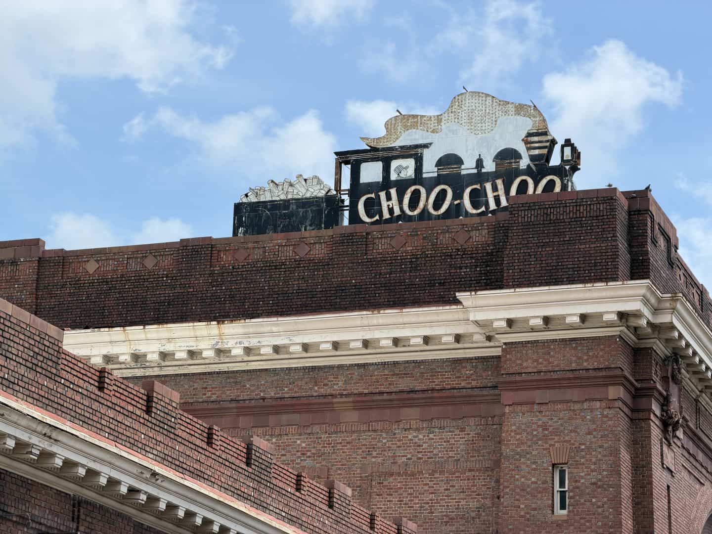 Weathered rooftop sign on a brick building reading CHOO-CHOO with a train silhouette against a blue sky.