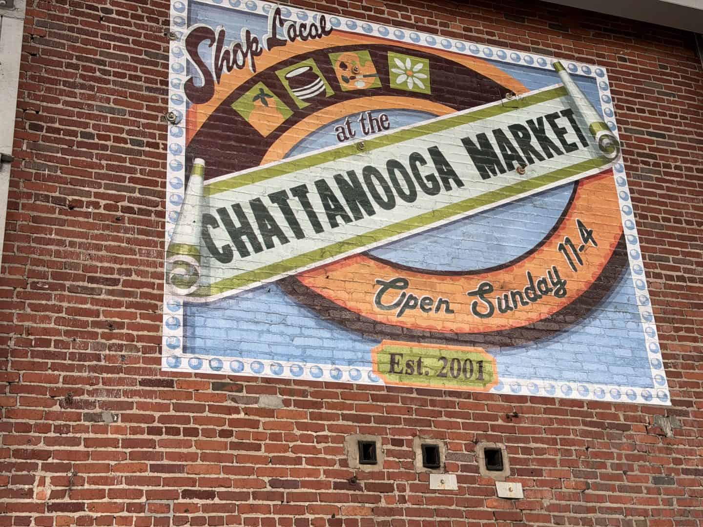 Colorful mural on a brick wall advertising Chattanooga Market, with bold lettering and decorative border showing an open Sundays message and est. 2001 text.