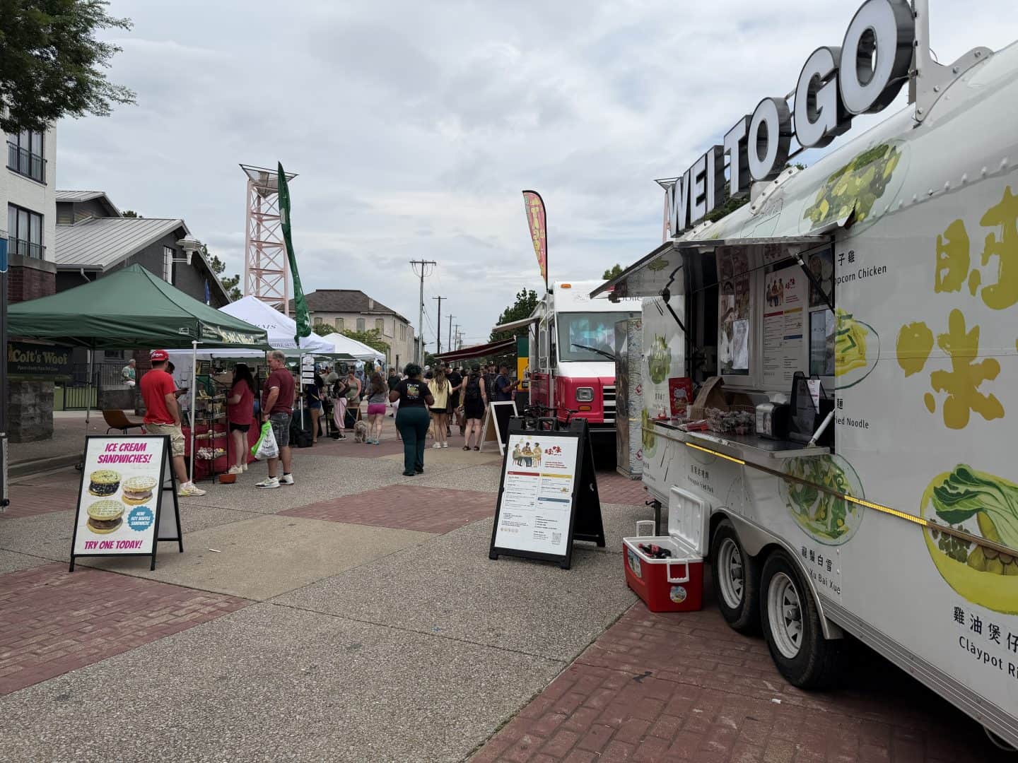 Outdoor street market with tents, stalls, and people browsing under a cloudy sky.