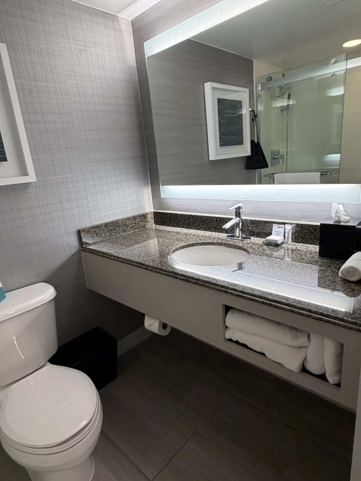 Modern bathroom with a granite countertop sink, large backlit mirror, and a white toilet nearby.