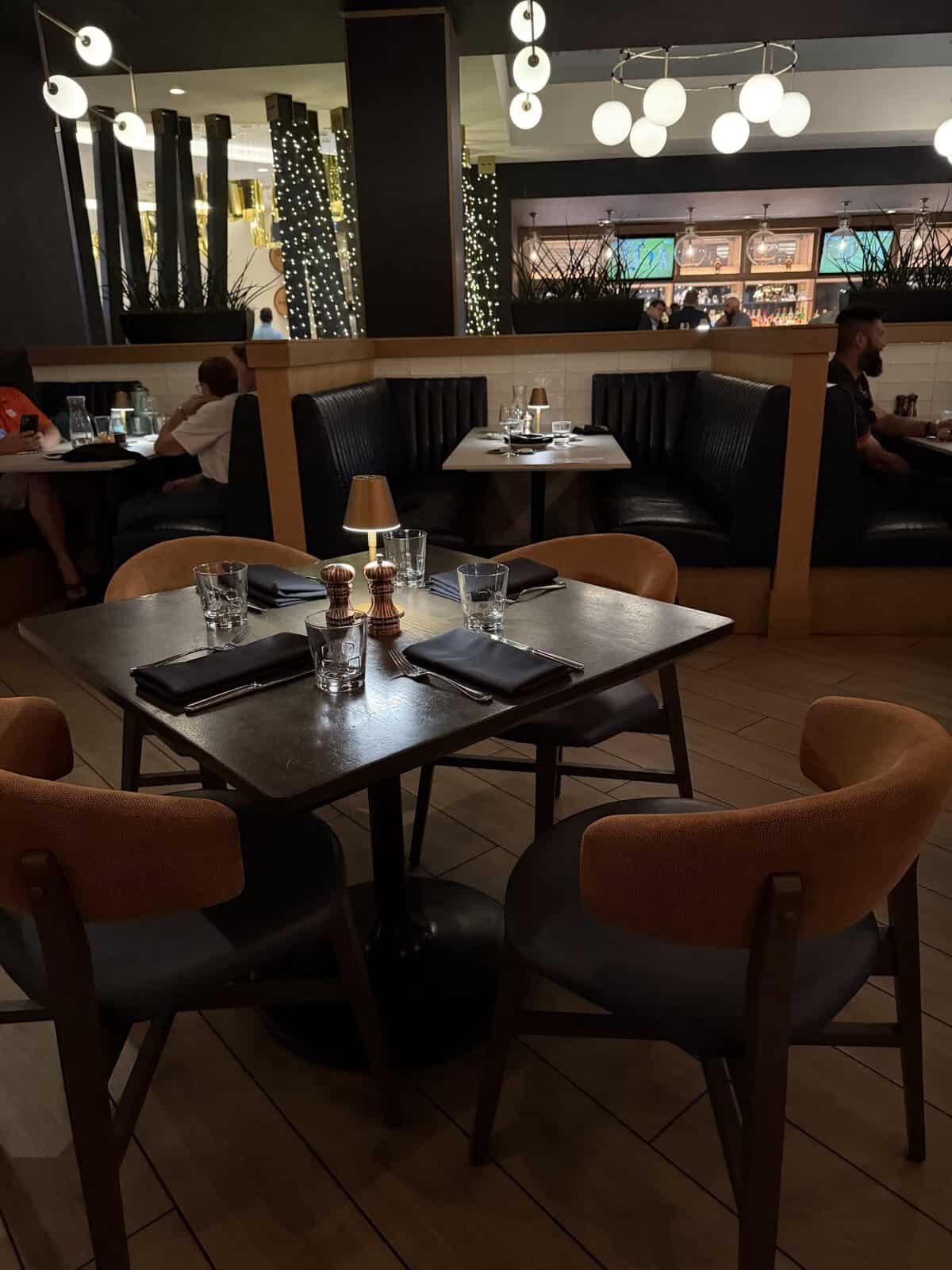 Restaurant dining area with dark leather booths, wooden tables, and dim lighting; tables set with glassware and napkins