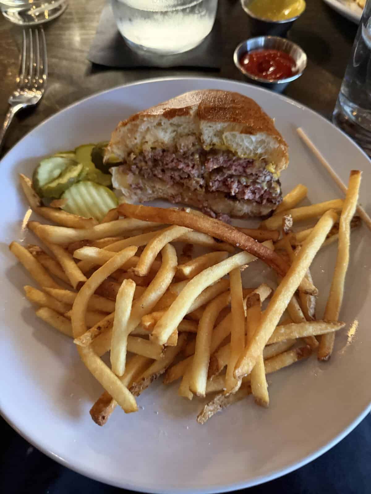 plate with half a cheeseburger, french fries and sliced pickles