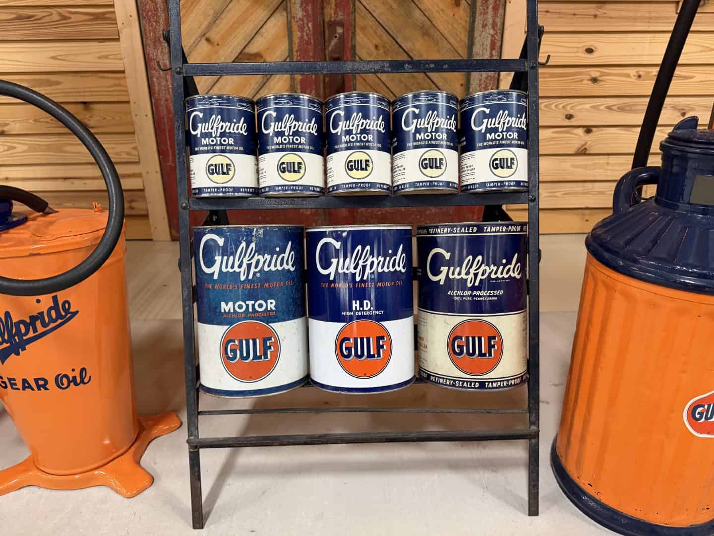 Shelf of Gulfpride motor oil cans in blue and white, with orange gear oil containers on either side and a wooden wall background.