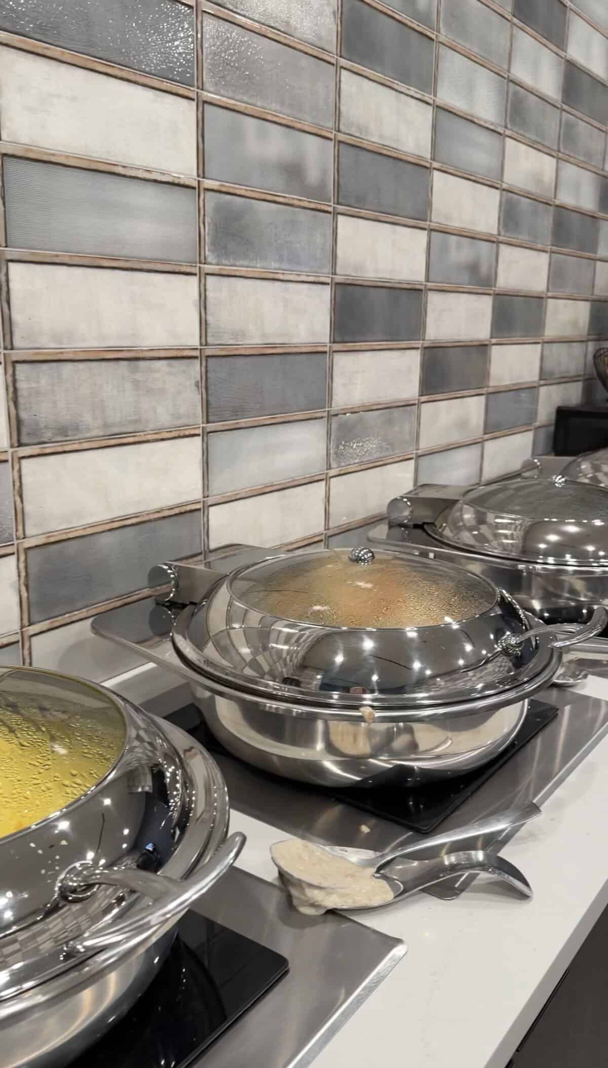 Screenshot - Adventures with Carli hotel buffett breakfast with row of hot foods in silver heating dishes