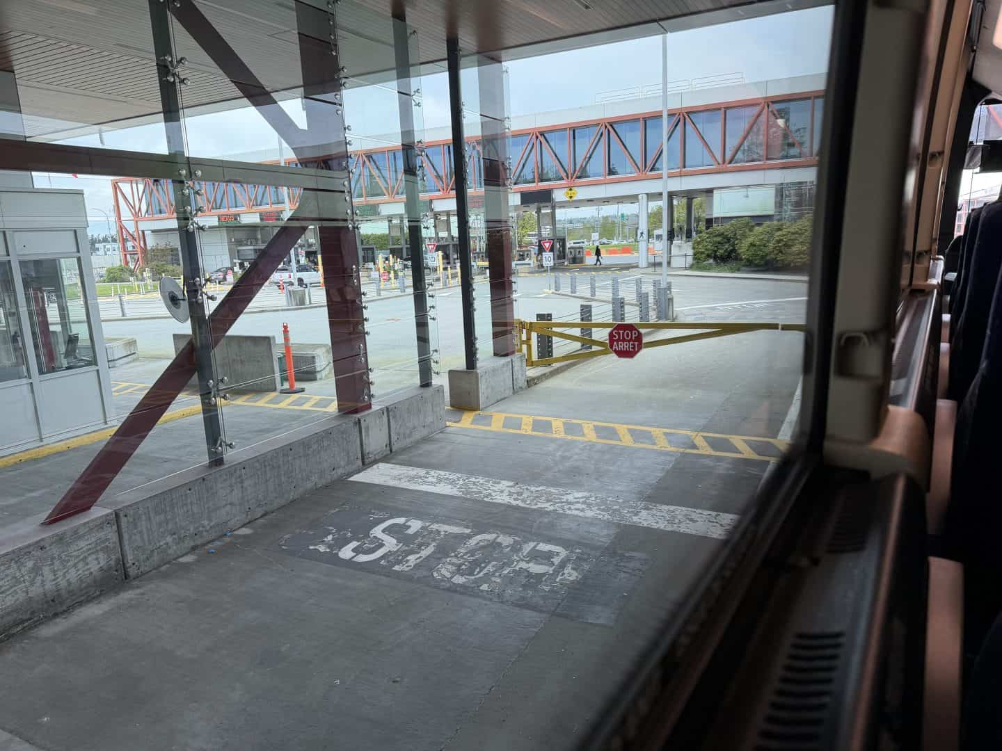 View from a bus doorway looking at a modern terminal: glass walls, red metal framework, and a stop sign ahead.