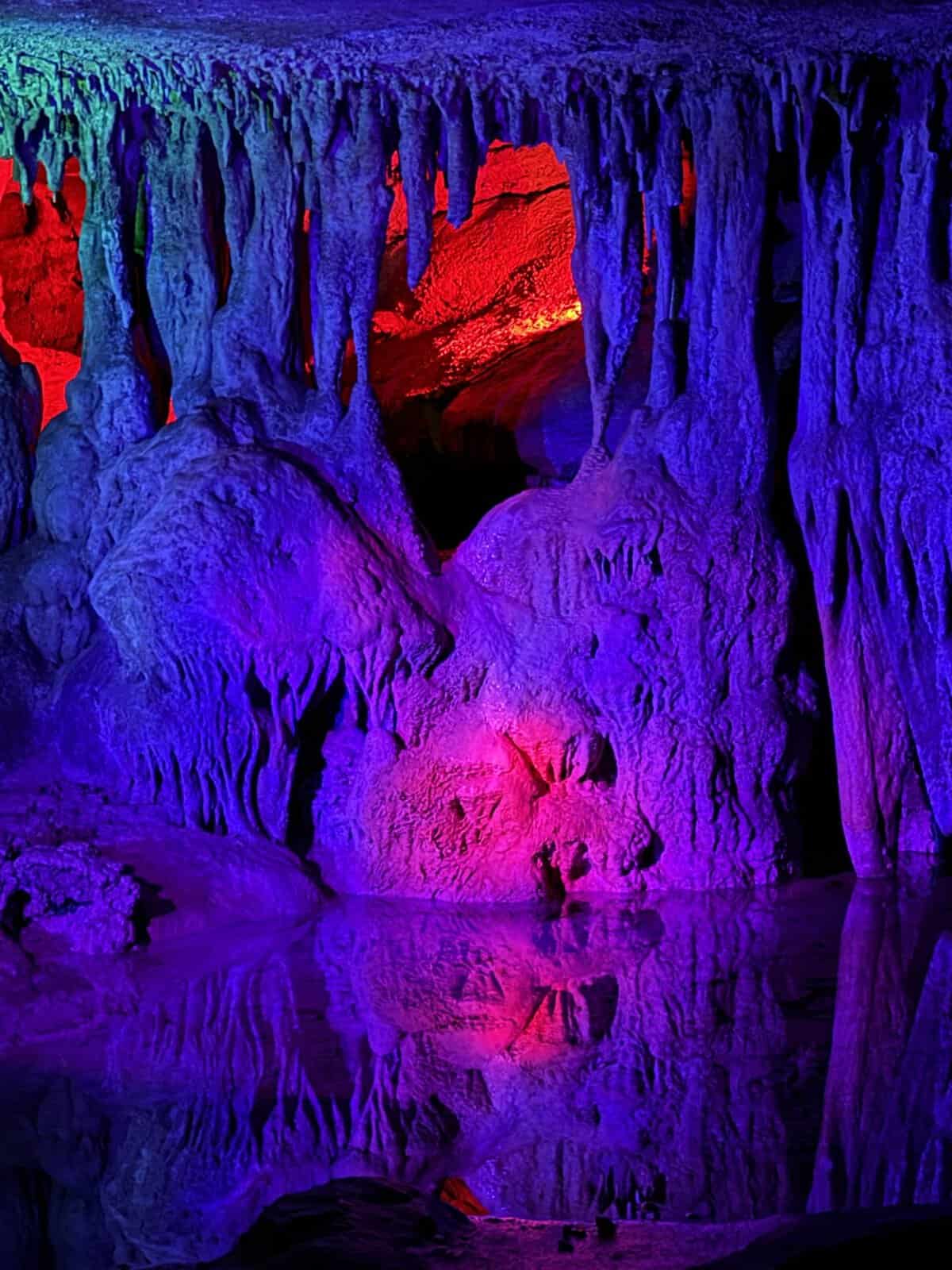 Cave interior with stalactites and stalagmites illuminated in blue, purple, and red lighting.