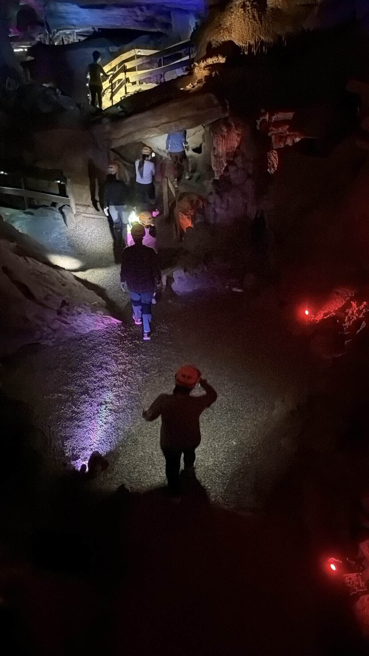 Group of people wearing helmets exploring a dark cave with wooden stairs and colorful lighting on Raccoon Mountain Caverns Wild Cave tour