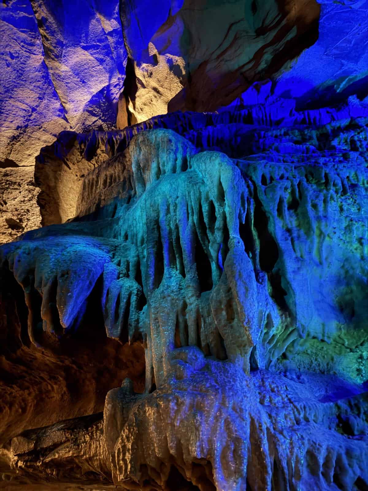 Colorful cave interior with stalactites and stalagmites illuminated in blue and amber light.