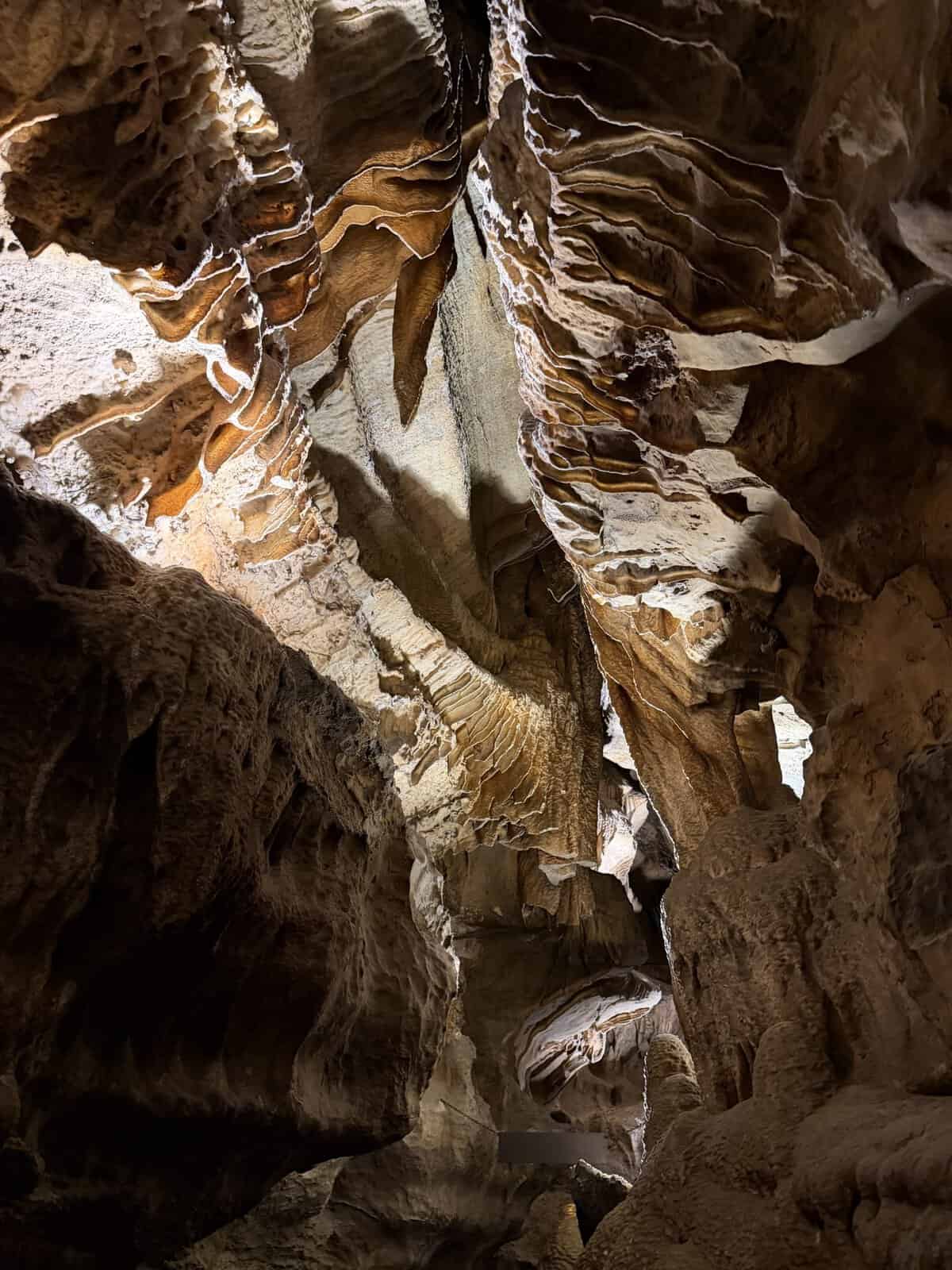 Rugged cave walls with layered, wavy rock formations and stalactite-like overhangs illuminated by warm light.