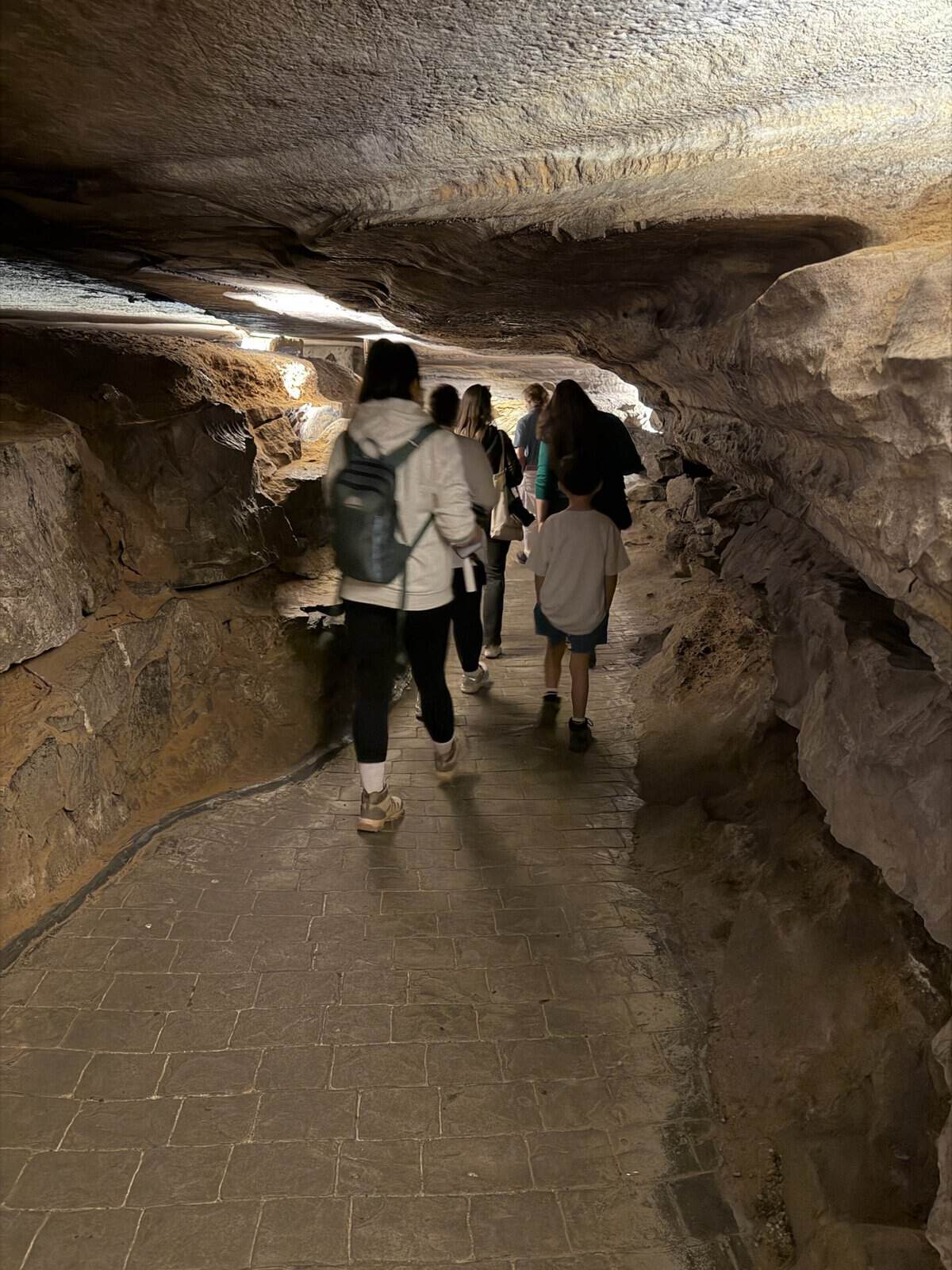 Group of people walking through a dim underground cave tunnel with rough rock walls on both sides.