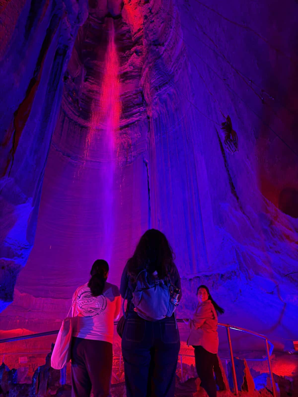 3 women looking at ruby falls undergound waterfall which is bathed in pink and purple light