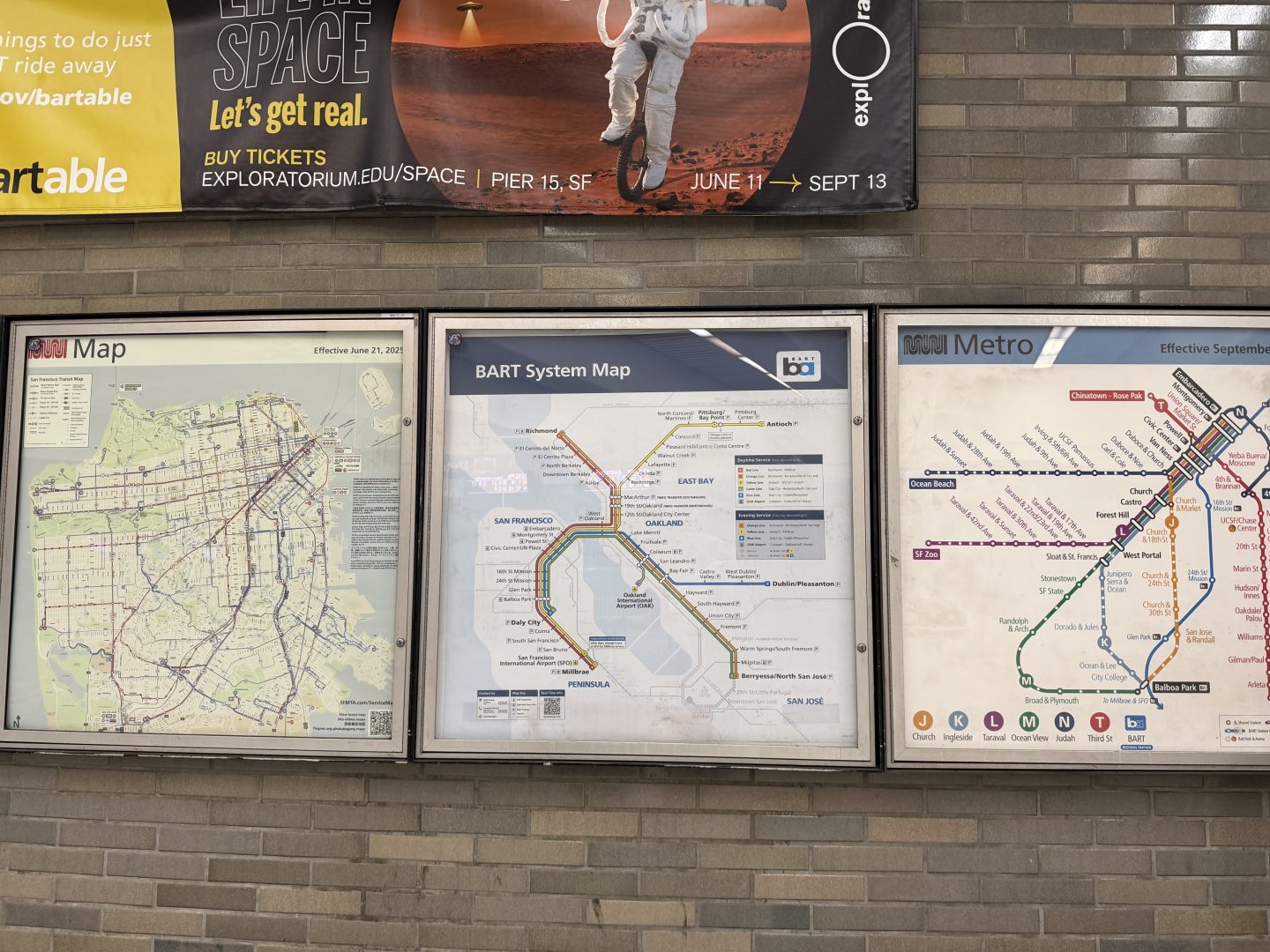san_francisco_bart map - Adventures with Carli Row of public transit maps in glass display frames mounted on a brick wall, with a large colorful banner above.