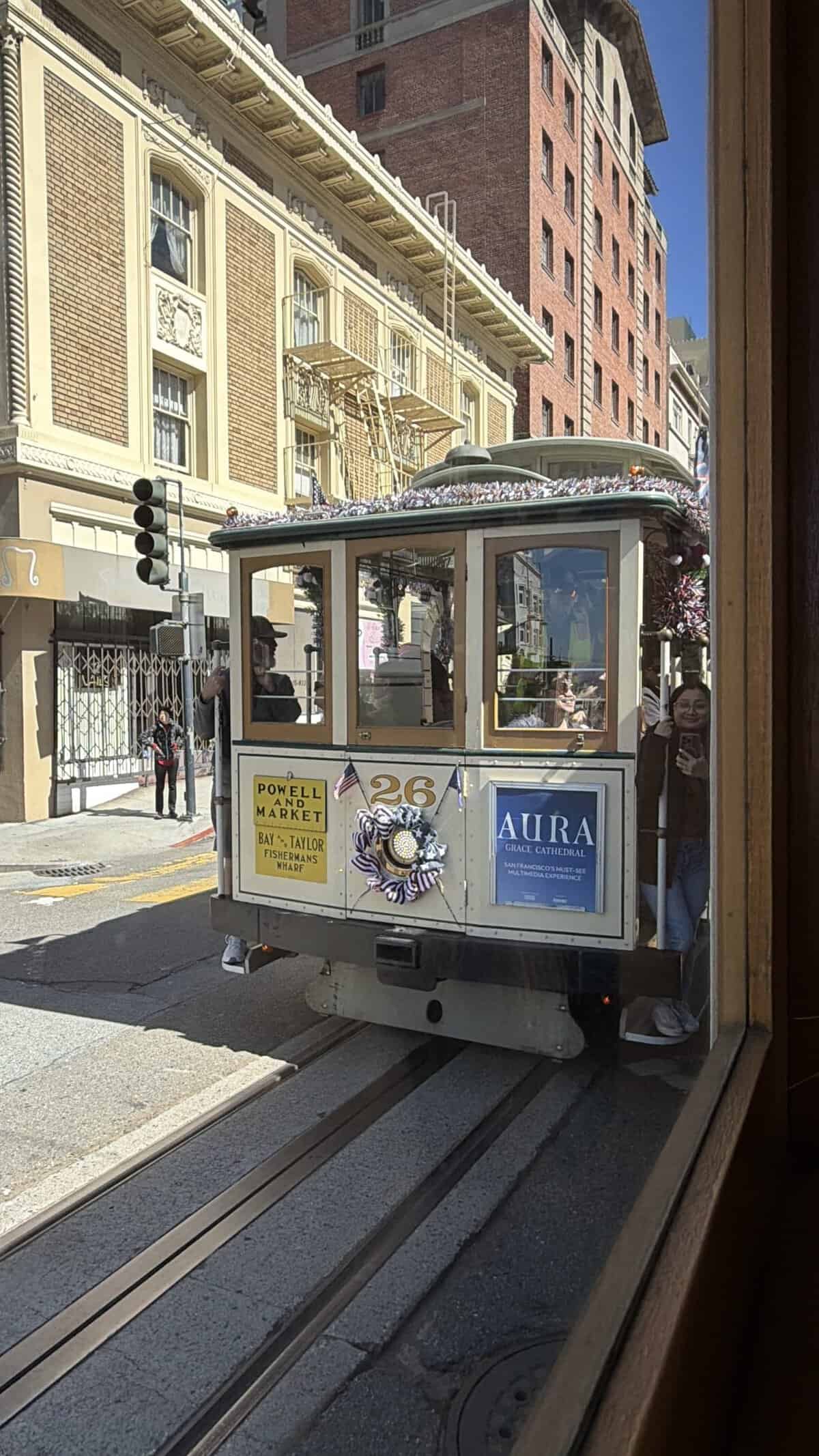 cable car in san francisco passing along the left side of window.  sign reads for powell and market line.