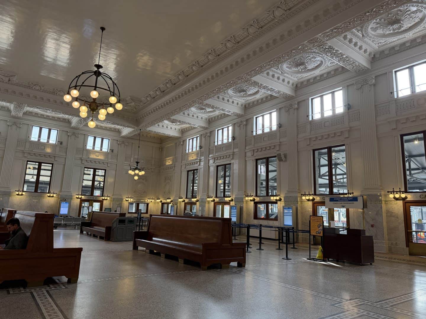 train station lobby interior with wood benches, a chandelier and white walls and coffered ceilings