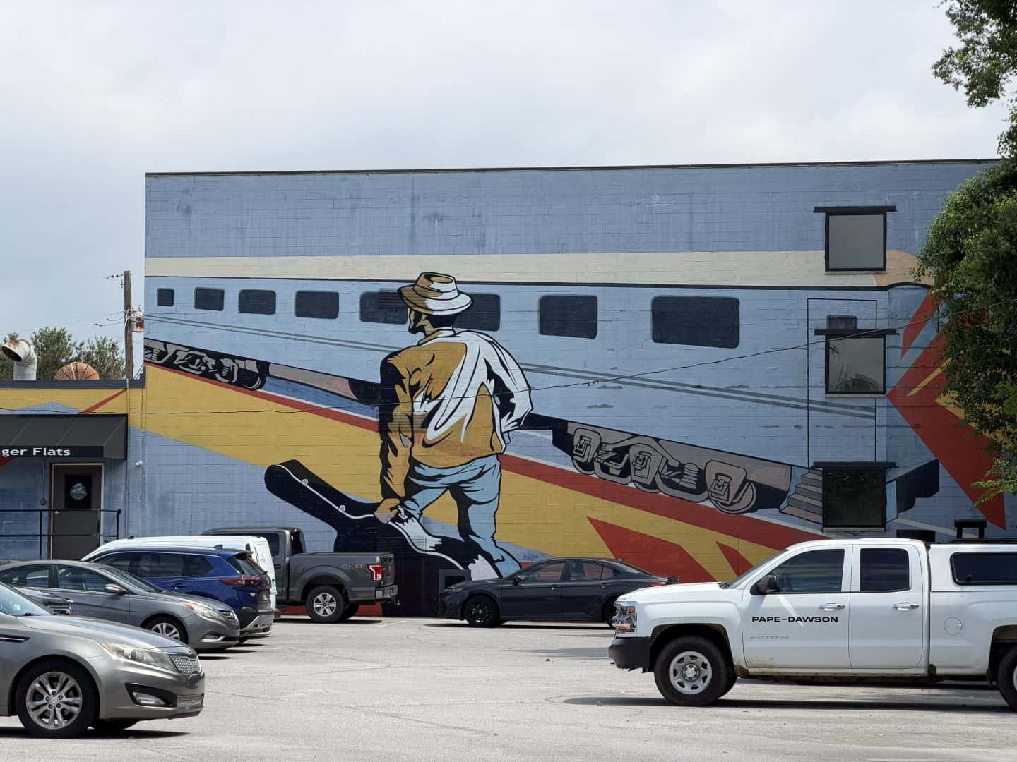 parking lot mural with man carrying guitar case walking along side a train