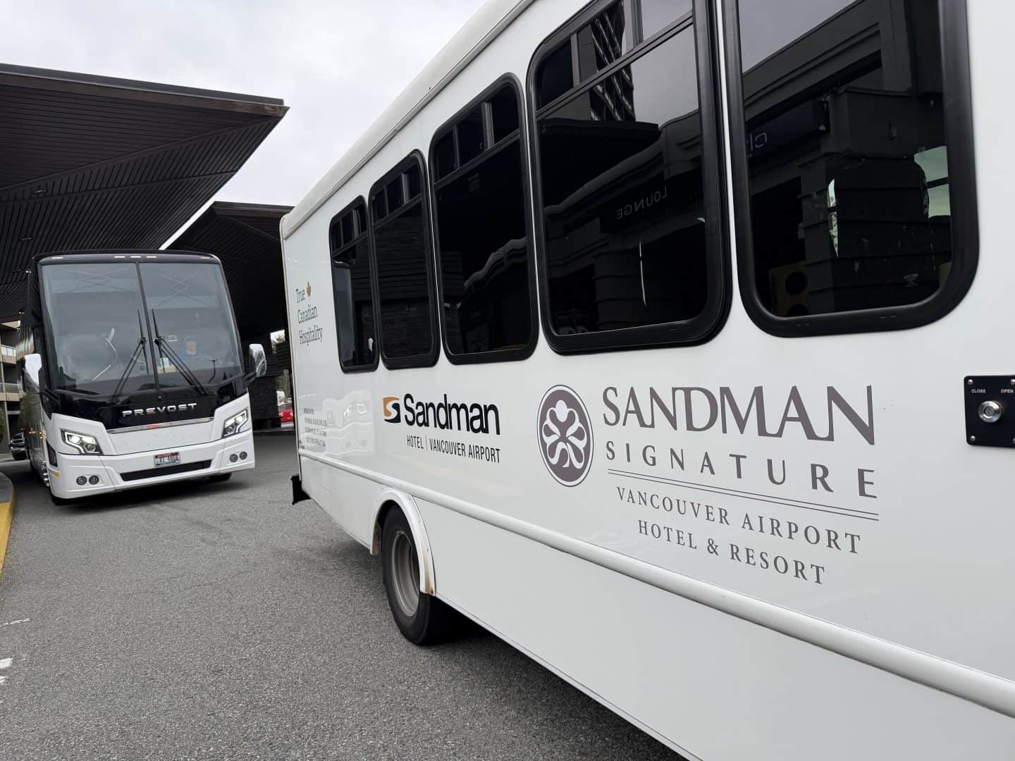 White tour bus with Sandman Signature branding parked at a Vancouver airport bus terminal.