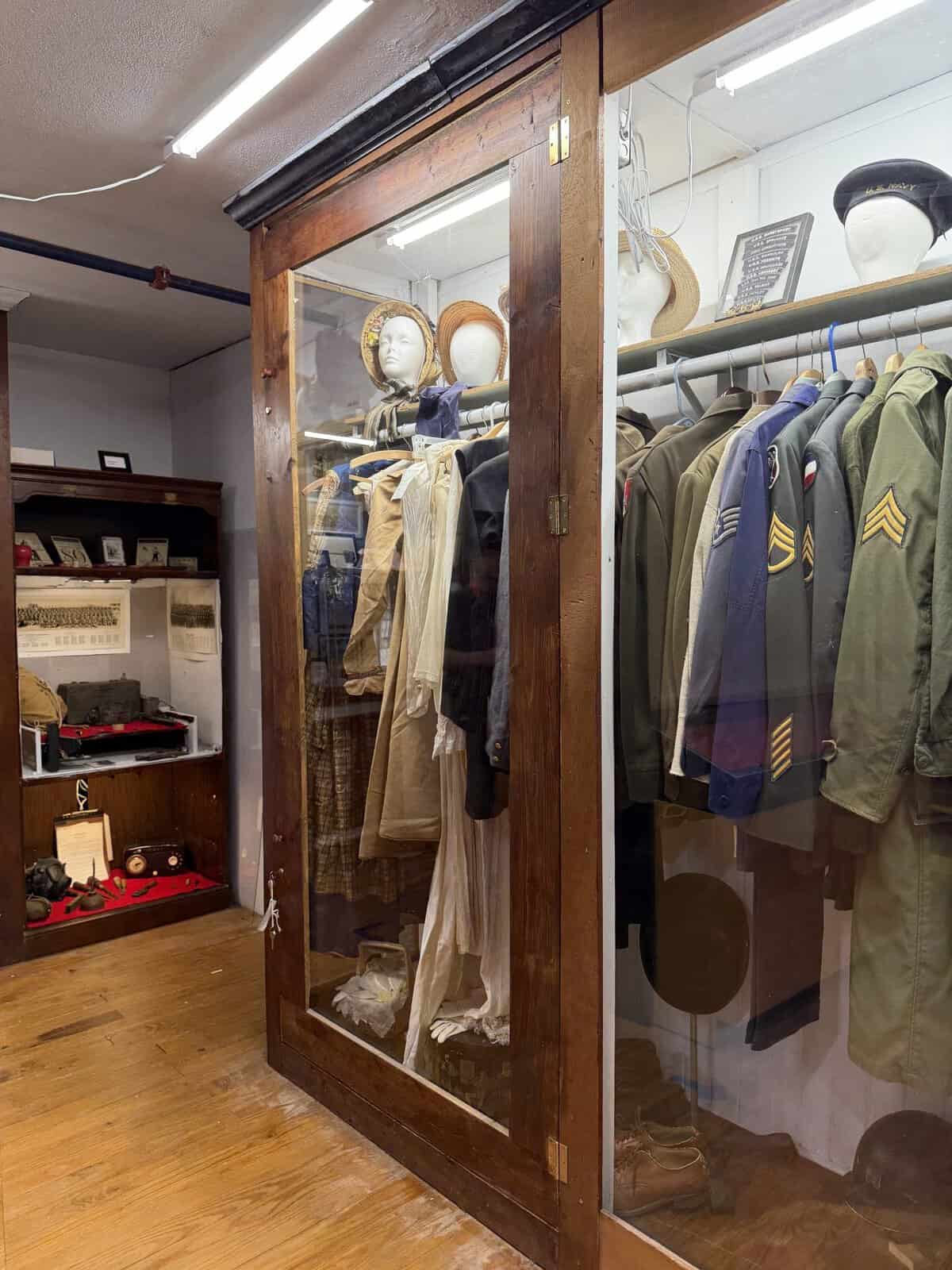 glass doored closet filled with vintage military jackets and women's bonnets 