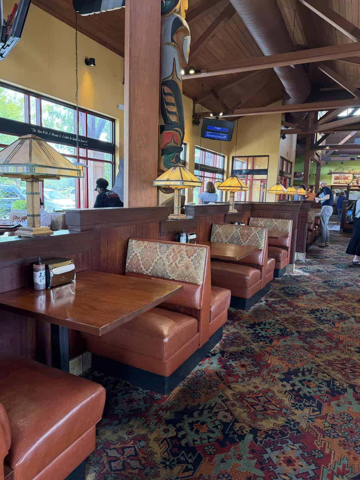 Interior of a casual diner with brown booths, wooden dividers, and warm pendant lamps along a patterned carpeted floor