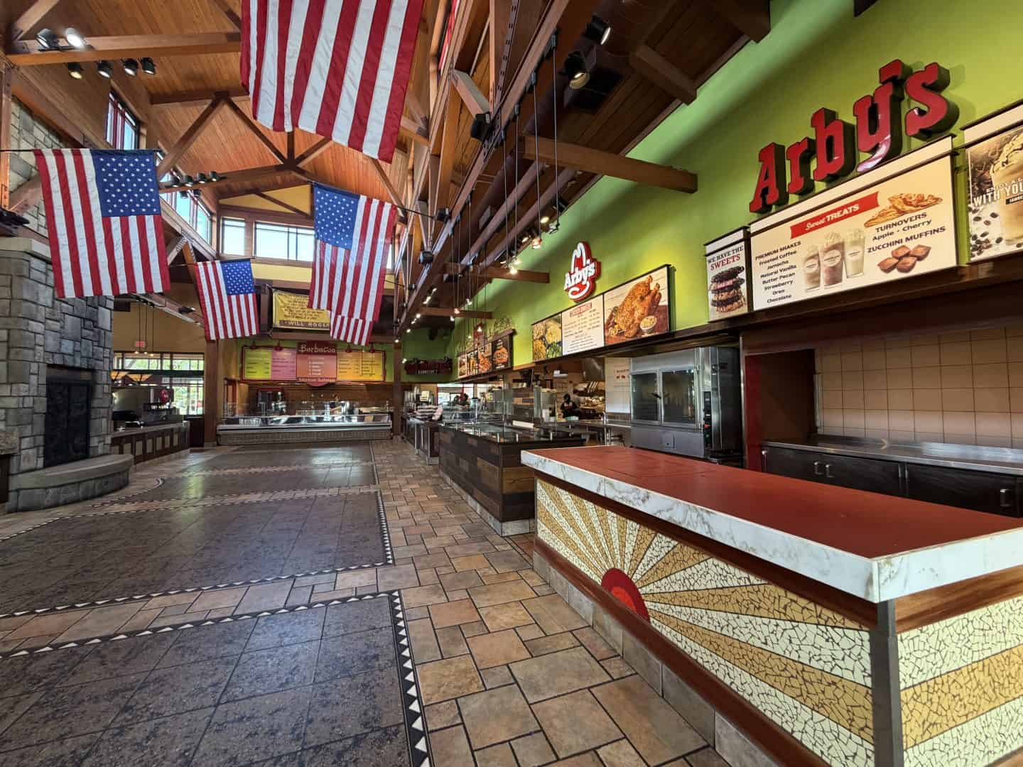 entrance of the world's largest Arby's with American flags hanging from a wooden ceiling and a green wall behind the counter area.