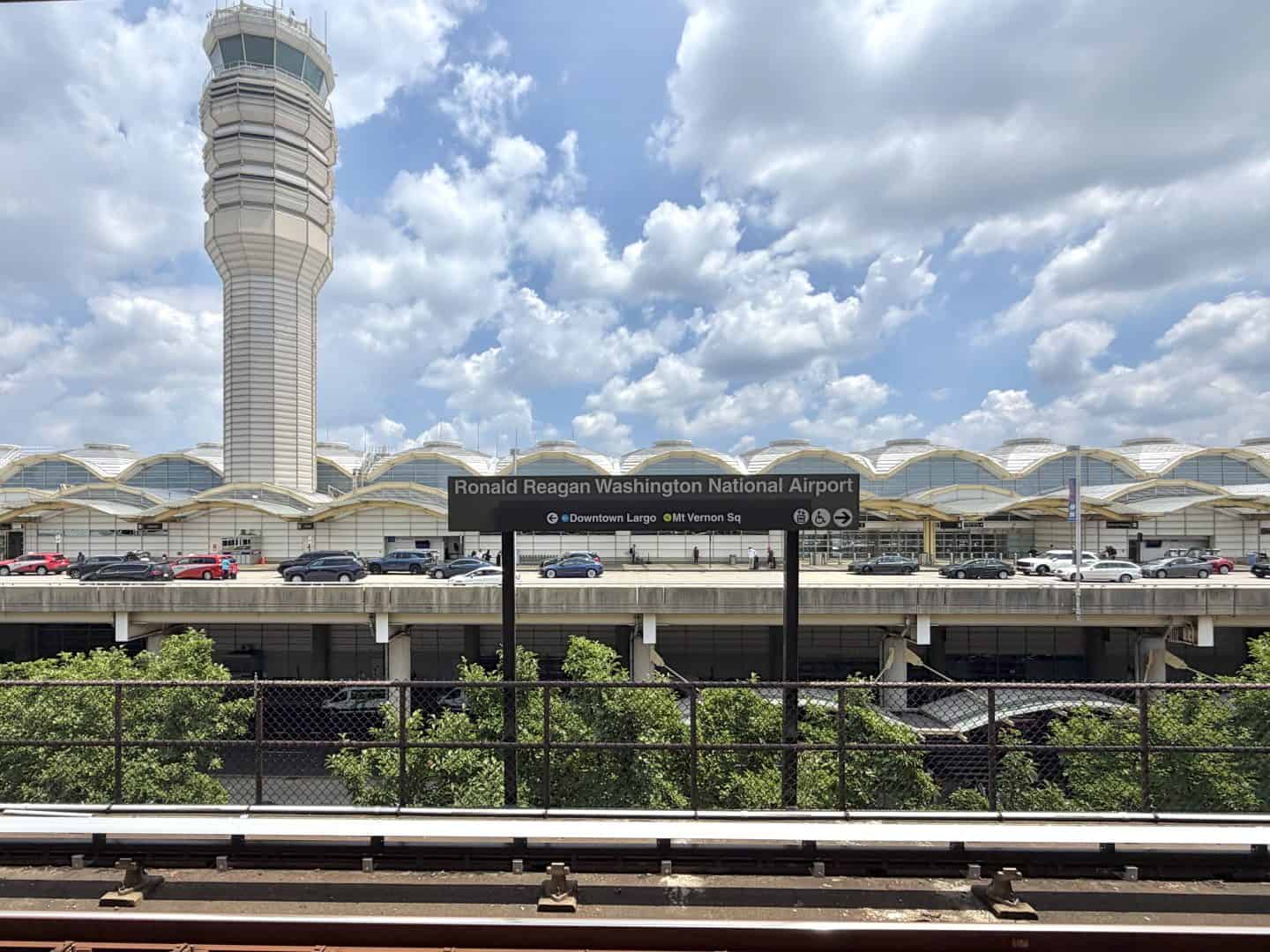 Control tower beside the Ronald Reagan Washington National Airport terminal under a cloudy blue sky.