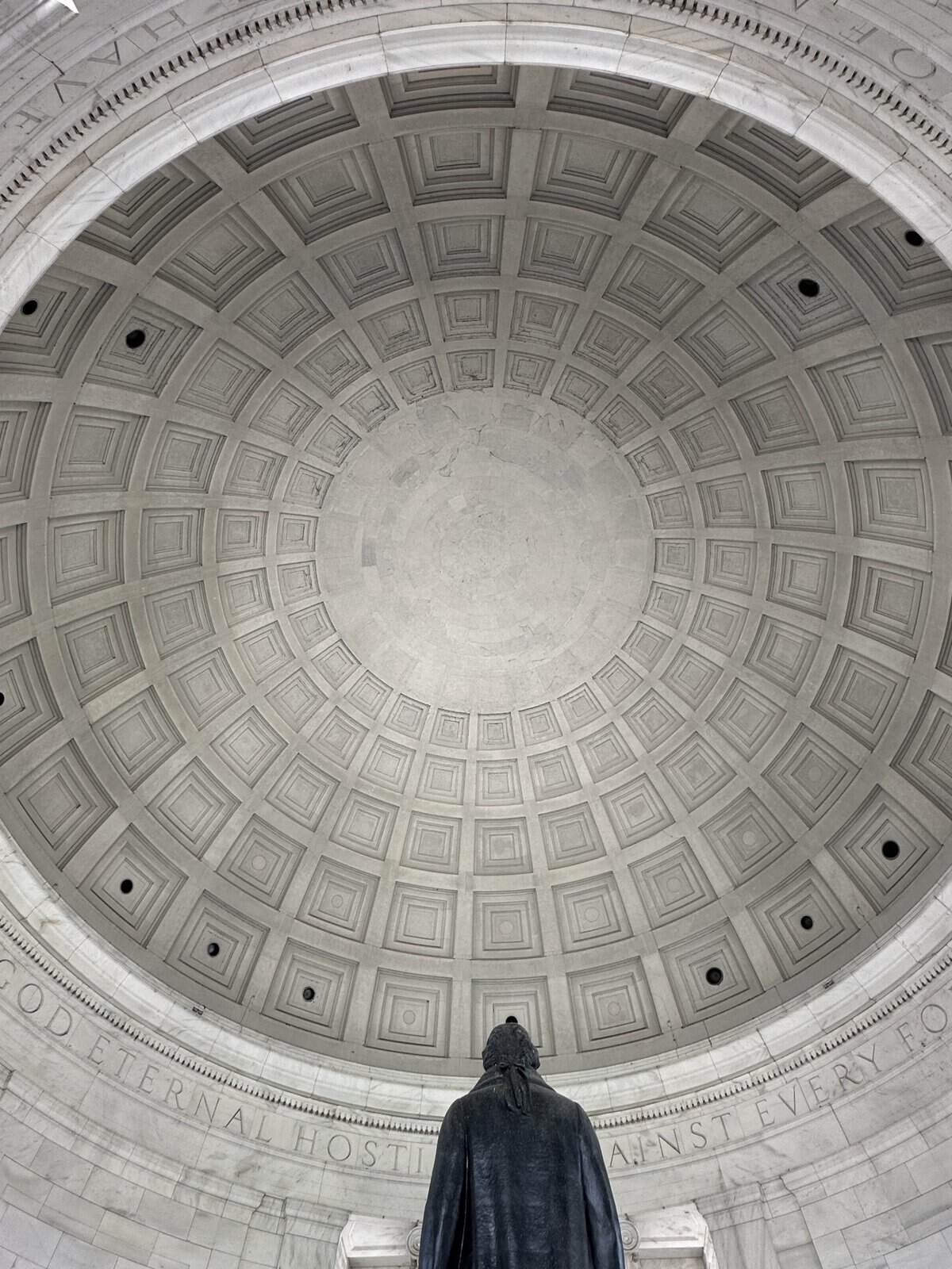 Interior of a large circular domed ceiling with square recessed panels and a robed statue of Thomas Jefferson standing at the base, viewed from in front.