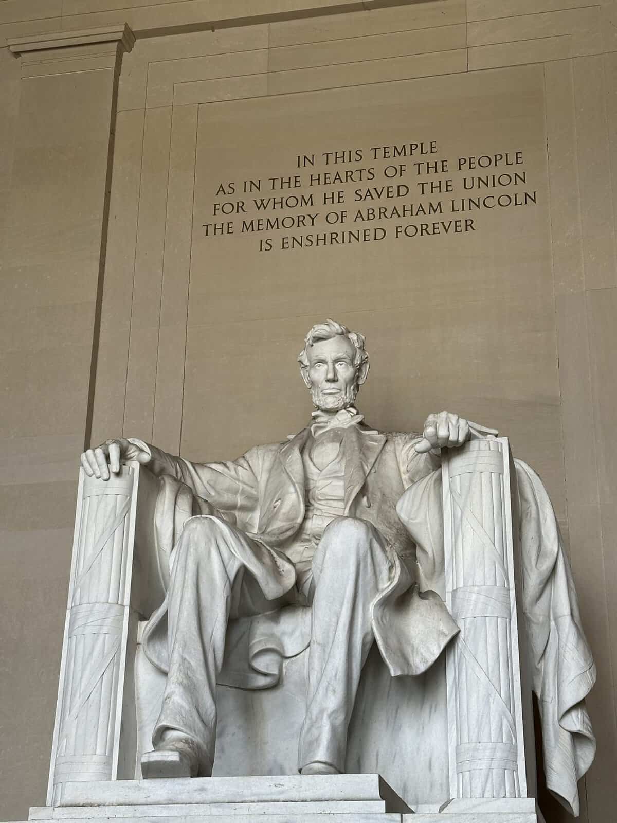 Seated marble statue of Abraham Lincoln in the Lincoln Memorial, with a carved inscription on the wall behind him.