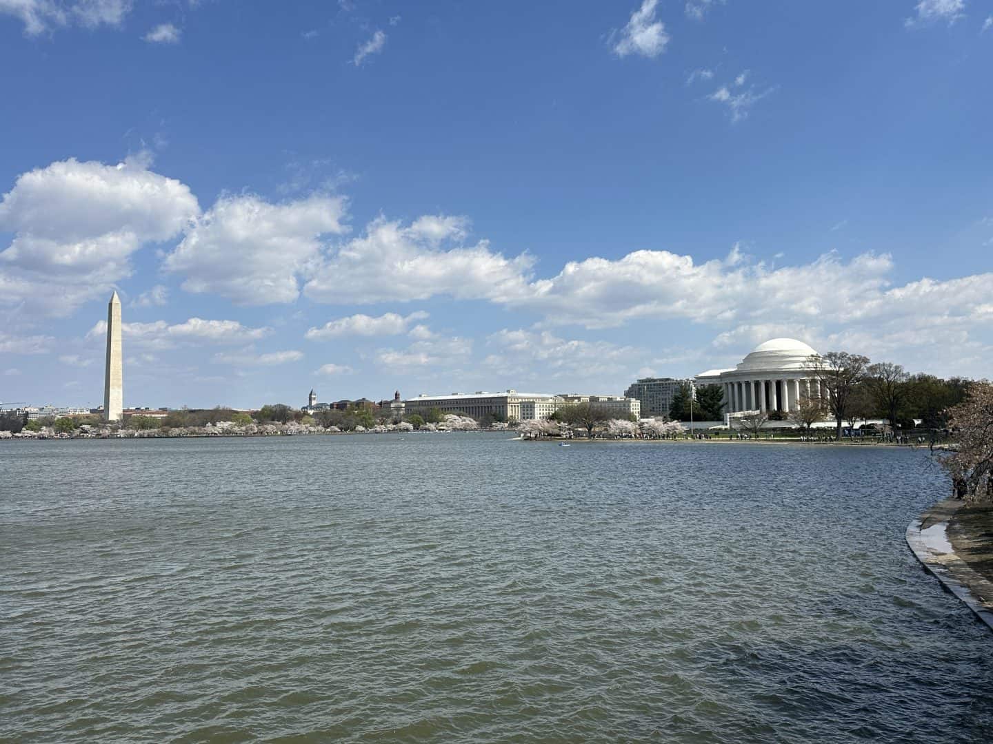 Waterfront view of the National Mall with the Washington Monument on the left and the Jefferson Memorial on the right under a blue sky with clouds.