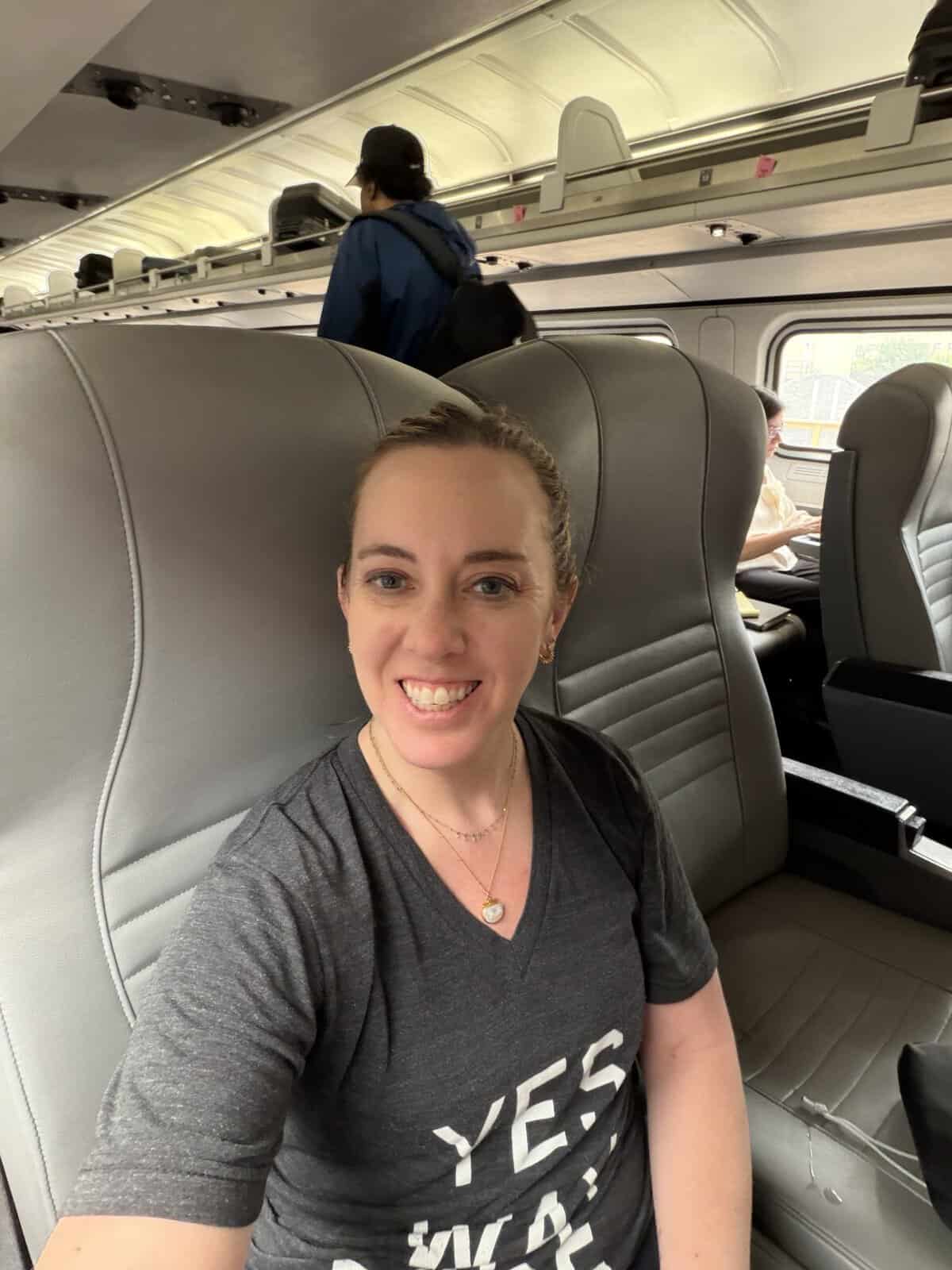 Carli taking a selfie on an airplane, with gray seats and overhead bins visible behind her.